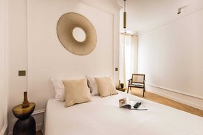 Ein ordentlich eingerichtetes Schlafzimmer mit einem Bett, Kissen, einem runden Spiegel, einem Sessel und einem Nachttisch.