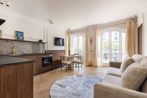 Eine moderne Küche mit Marmorarbeitsplatte, Holzschränken und einem eingebauten Ofen. Es gibt einen Essbereich mit rundem Tisch und Stühlen sowie ein Sofa im Wohnzimmer.