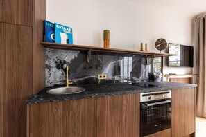 Eine moderne Küche mit Marmor-Spritzschutz, Holzschränken, einem Einbauofen und einer Edelstahl-Spüle.