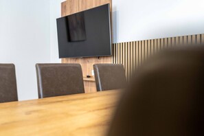 A conference room with a large flat-screen TV mounted on a wooden wall, a wooden table, and four chairs. - Maiskogelblick Apartments - TOP 7, Terrace & Sauna (Piesendorf)