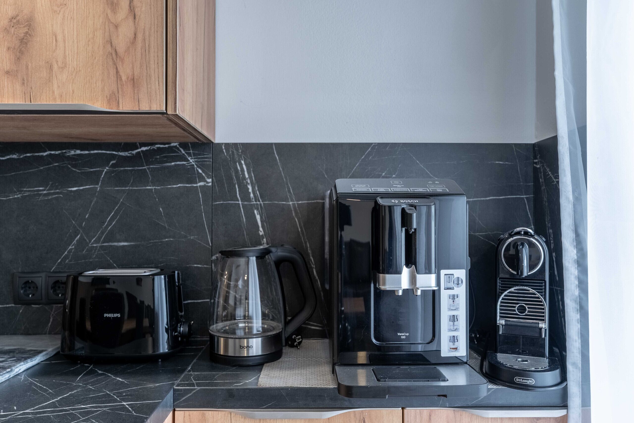 A kitchen with a coffee maker, toaster, and glass carafe on a marble countertop.