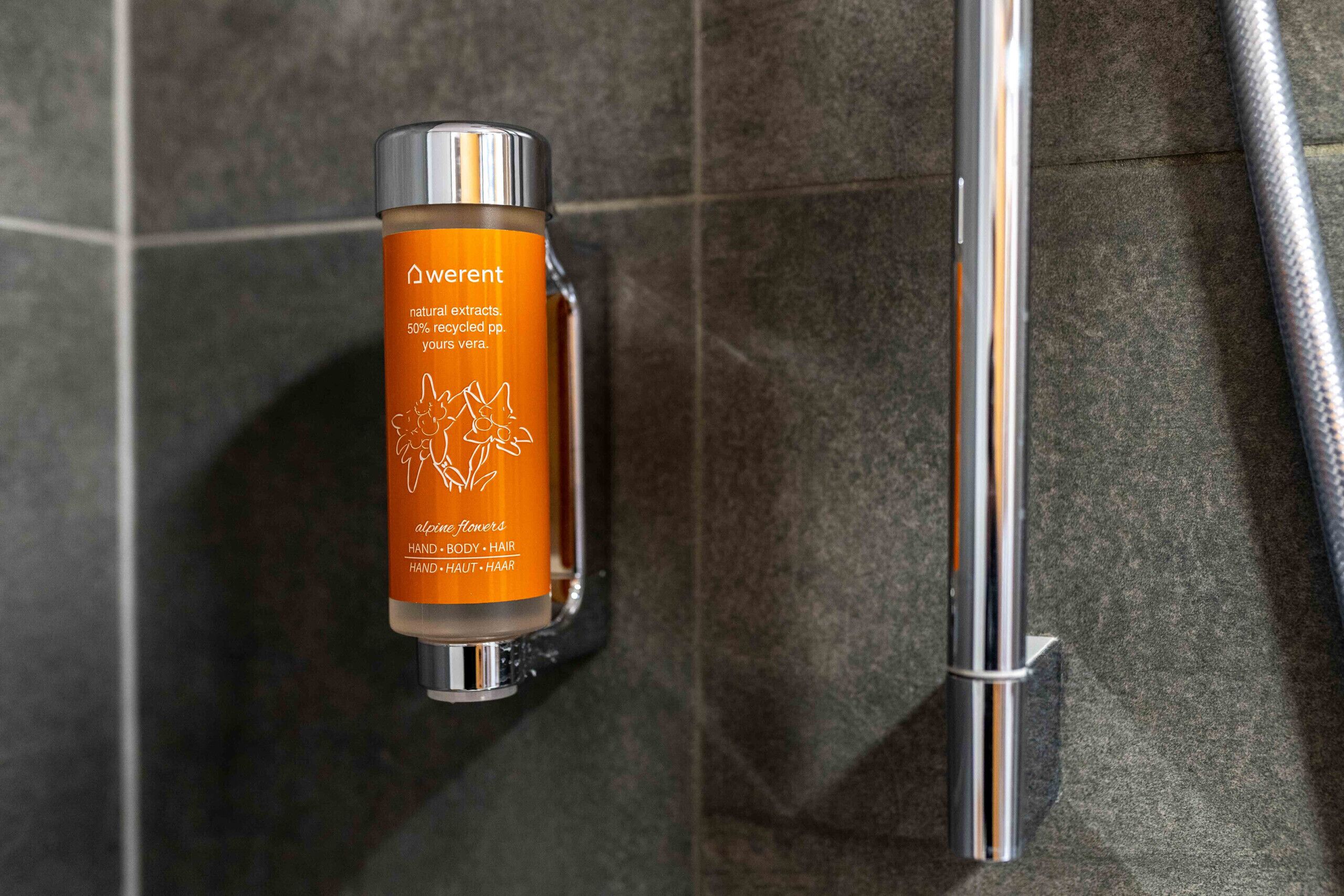 Un espace douche équipé d’un flacon de gel douche Weren’t et d’un pommeau de douche chromé.
