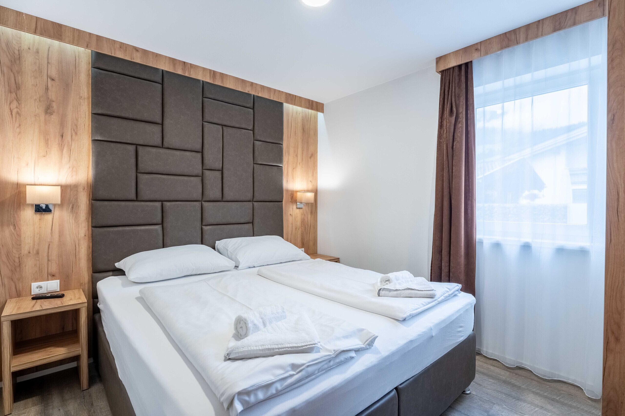 Ein modernes Hotelzimmer mit einem großen Bett, Nachttischen und einem Kopfteil mit geometrischem Muster.