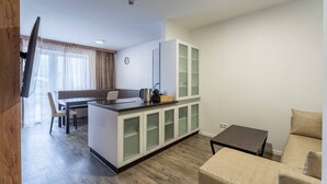 Un salon moderne comprenant un canapé, une table basse, un coin cuisine avec une table à manger et des chaises, et un téléviseur fixé au mur.