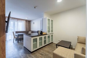 A modern living room with a sofa, a coffee table, a kitchen area with a dining table and chairs, and a TV mounted on the wall. - Maiskogelblick Apartments - TOP 11 (Piesendorf)