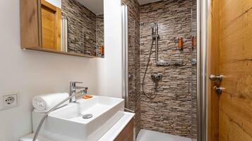Une salle de bain avec un lavabo blanc, une douche avec un mur en pierre et une porte en bois.