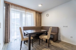 Ein Essbereich mit Holztisch und Stühlen, einer Bank, einem Fenster mit Vorhängen und einer Wanduhr.