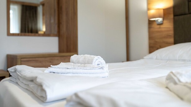 Un lit bien fait, avec des serviettes blanches pliées, une tête de lit en bois et un luminaire fixé au mur.
