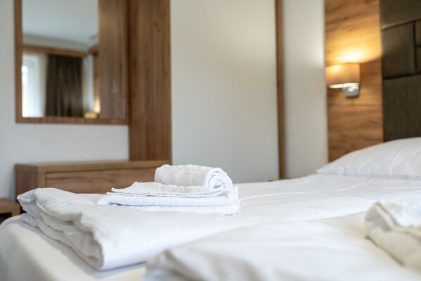 A neatly made bed with folded white towels, a wooden headboard, and a wall-mounted light fixture. - Maiskogelblick Apartments - TOP 11 (Piesendorf)