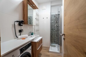 Ein modernes Badezimmer mit Glasdusche, Waschmaschine, Spiegel und Handtuchhalter.