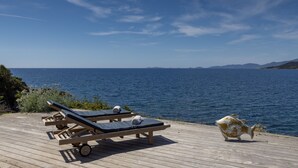 Eine Holzterrasse mit zwei Liegestühlen und einer dekorativen Fischskulptur am Meer.