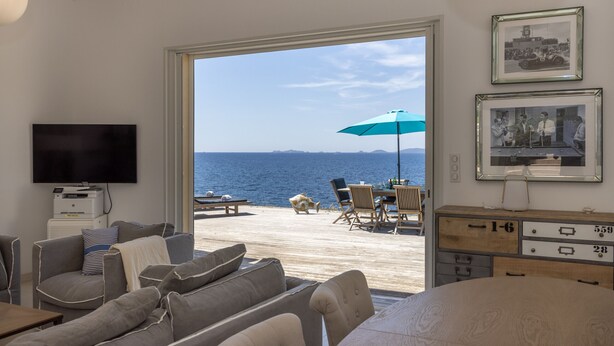 Ein Wohnzimmer mit Fernseher, Sofa und Meerblick durch eine Glastür.