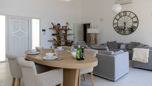 Ein modernes Wohnzimmer mit einem runden Esstisch, grauen Sofas und einer großen Wanduhr.