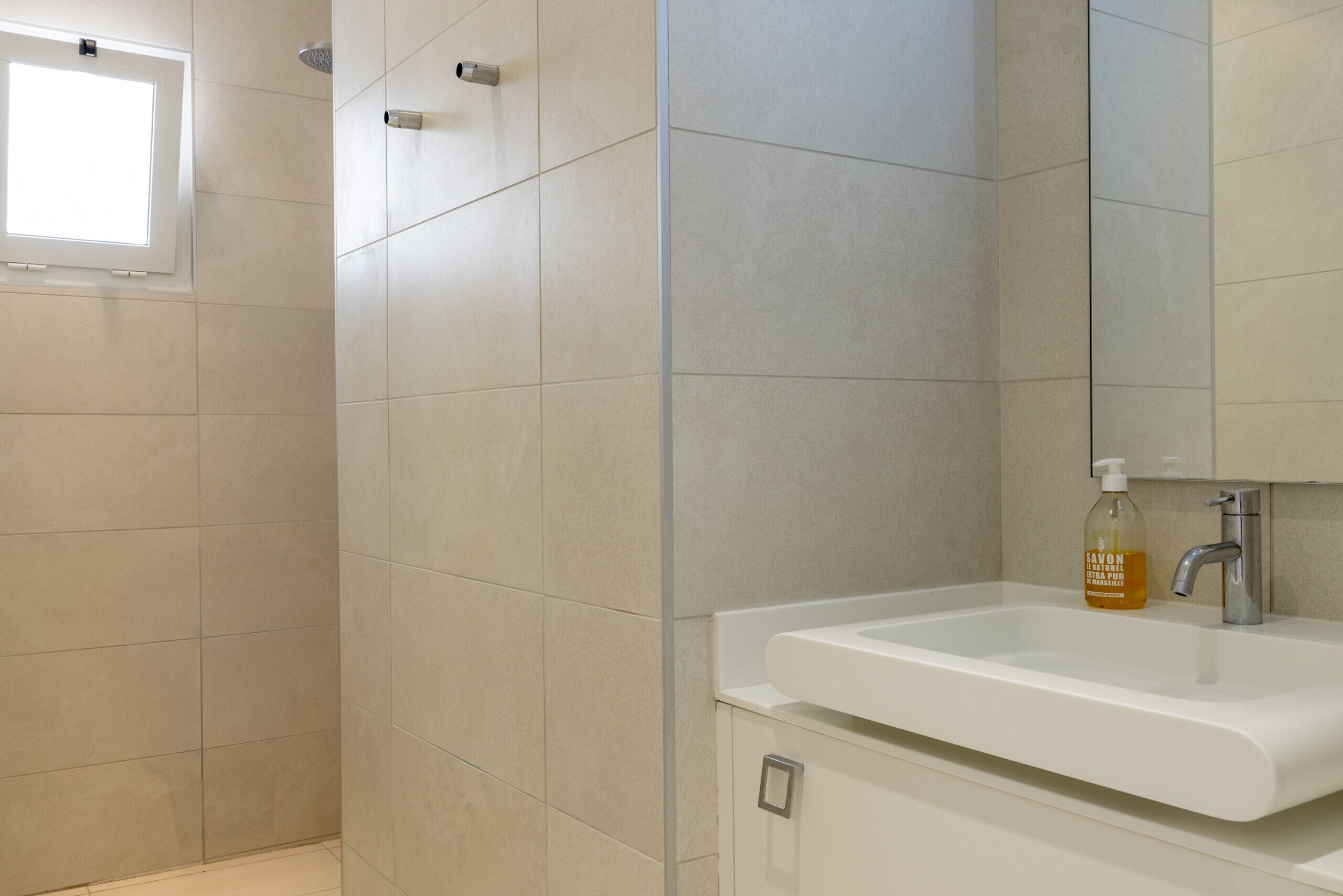 A bathroom with a white sink, a mirror, and a shower area.
