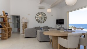 Ein modernes Wohnzimmer mit einer großen Uhr, einem Fernseher und Blick auf das Meer.