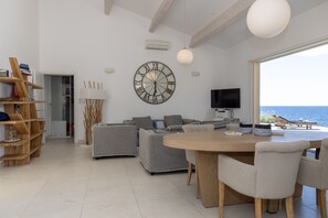 Ein modernes Wohnzimmer mit einer großen Uhr, einem Fernseher und Blick auf das Meer.