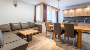 Un salon moderne comprenant un canapé, une table à manger, des chaises et un coin cuisine avec des meubles en bois et un dosseret en marbre.