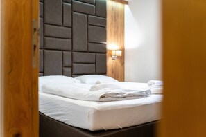 A neatly made bed with white linens, a headboard with a geometric pattern, and a wall-mounted light fixture. - Maiskogelblick Apartments - TOP 8, Balcony & Sauna (Piesendorf)