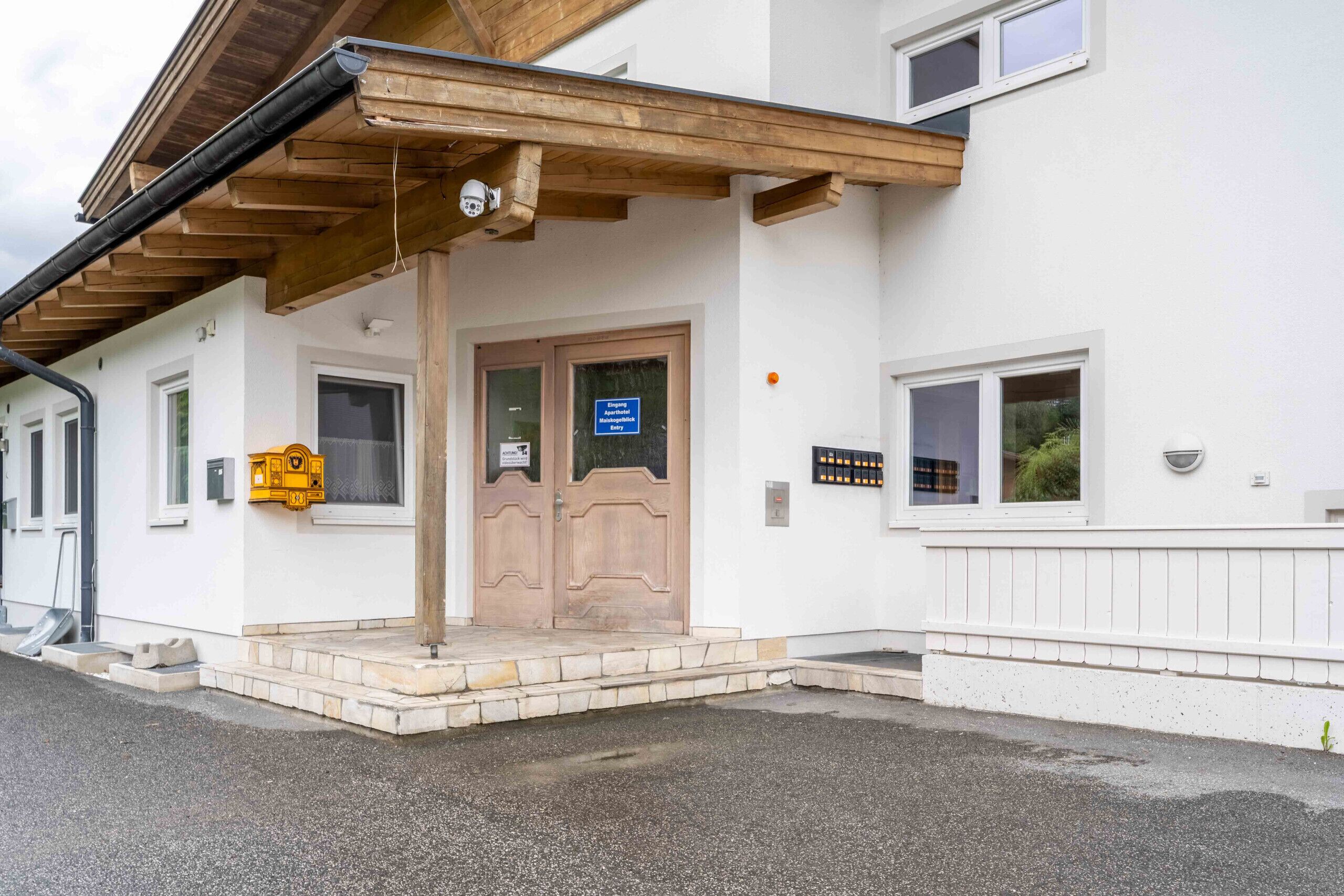 Un bâtiment doté d’un porche en bois, d’une porte avec une enseigne et d’une petite boîte aux lettres jaune.