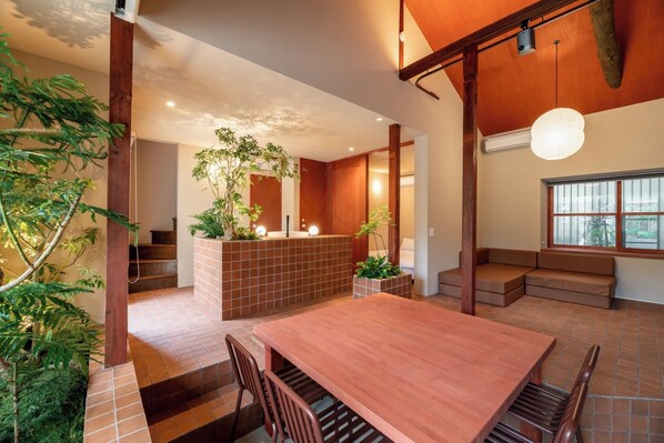 Ein modernes Interieur mit Holztisch, gepolsterten Sitzmöglichkeiten, einer kleinen Rezeption und einer Treppe, die eine weitere Ebene hinaufführt.