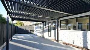 A covered outdoor patio area with a concrete floor, a wooden fence, and a white wall with windows. - Russley home near the airport, single level with parking (Christchurch)