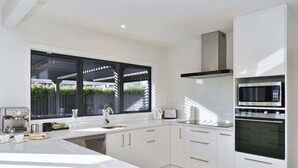 A modern kitchen with white cabinetry, a large window, and built-in appliances. - Russley home near the airport, single level with parking (Christchurch)