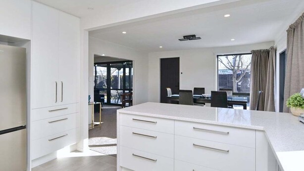 A modern kitchen with white cabinetry, a large island, and a dining area with a table and chairs. - Russley home near the airport, single level with parking (Christchurch)