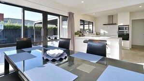A modern kitchen with a microwave, oven, and a dining area with a glass table and chairs. - Russley home near the airport, single level with parking (Christchurch)