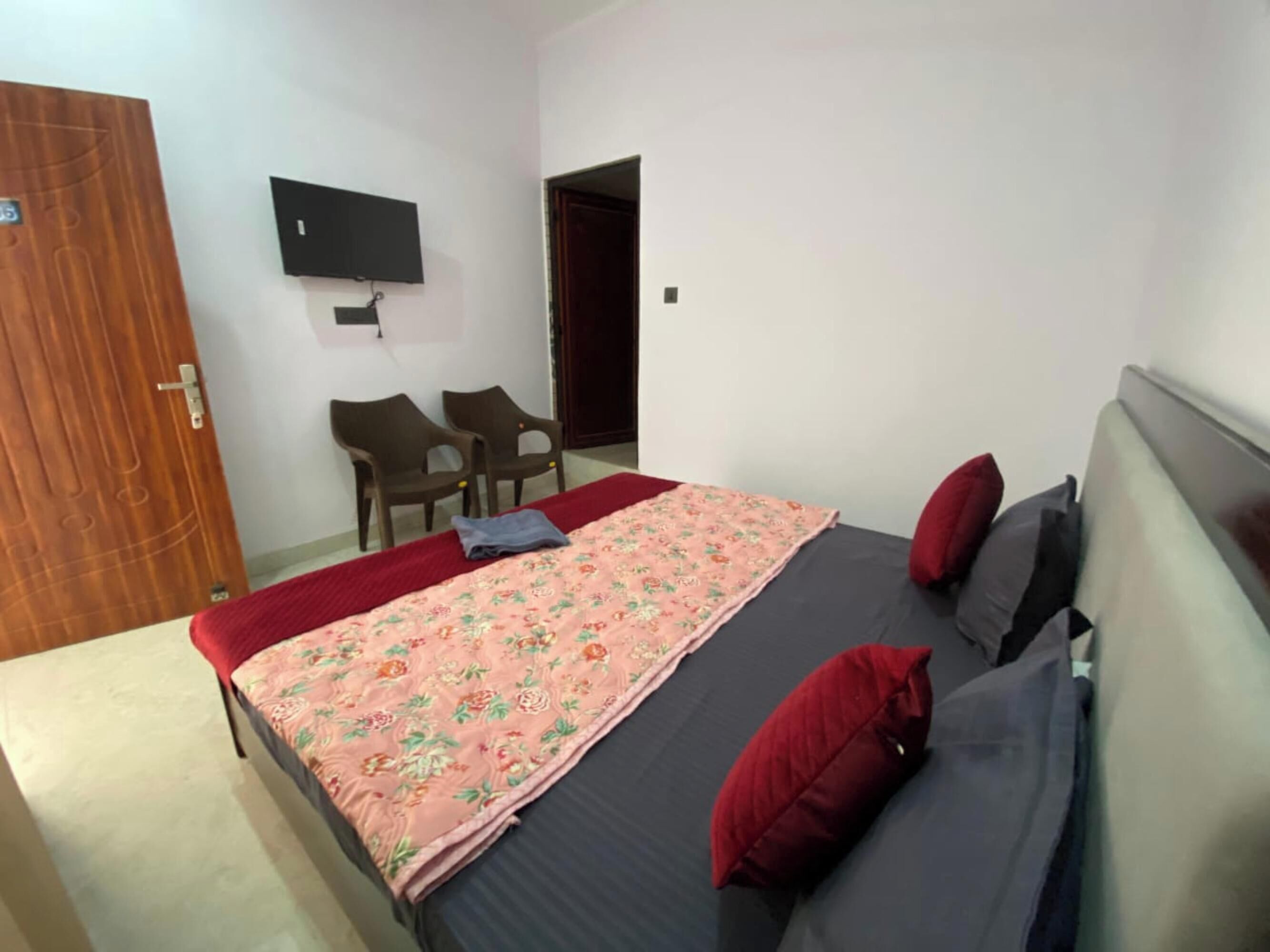 Ein Schlafzimmer mit einem Bett, einem an der Wand montierten Fernseher, zwei Sesseln und einer Tür.