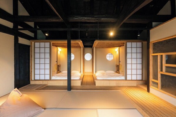 Ein traditioneller japanischer Raum mit Tatami-Bodenbelag, zwei Tatami-Matten, einer niedrigen Holzplattform und einer Schiebetür mit rundem Fenster.