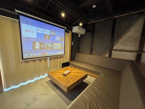 Ein Zimmer mit einem großen Bildschirm, der Streaming-Dienste zeigt, einem Holztisch und einer gepolsterten Sitzecke.