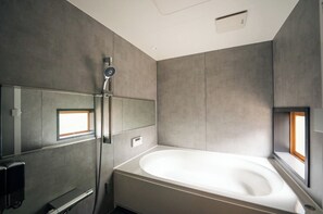 Ein modernes Badezimmer mit einer freistehenden Badewanne, einer Handbrause und einem großen Spiegel.