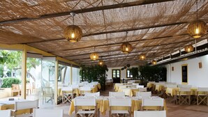 Un ristorante con tavoli apparecchiati, un tetto in paglia e lampadari a sospensione.