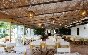 A restaurant with tables set for dining, a thatched roof, and hanging pendant lights.