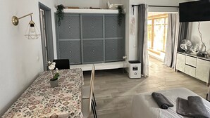 Una camera compatta con un tavolo da pranzo, sedie, un letto, una TV e una finestra con tende.