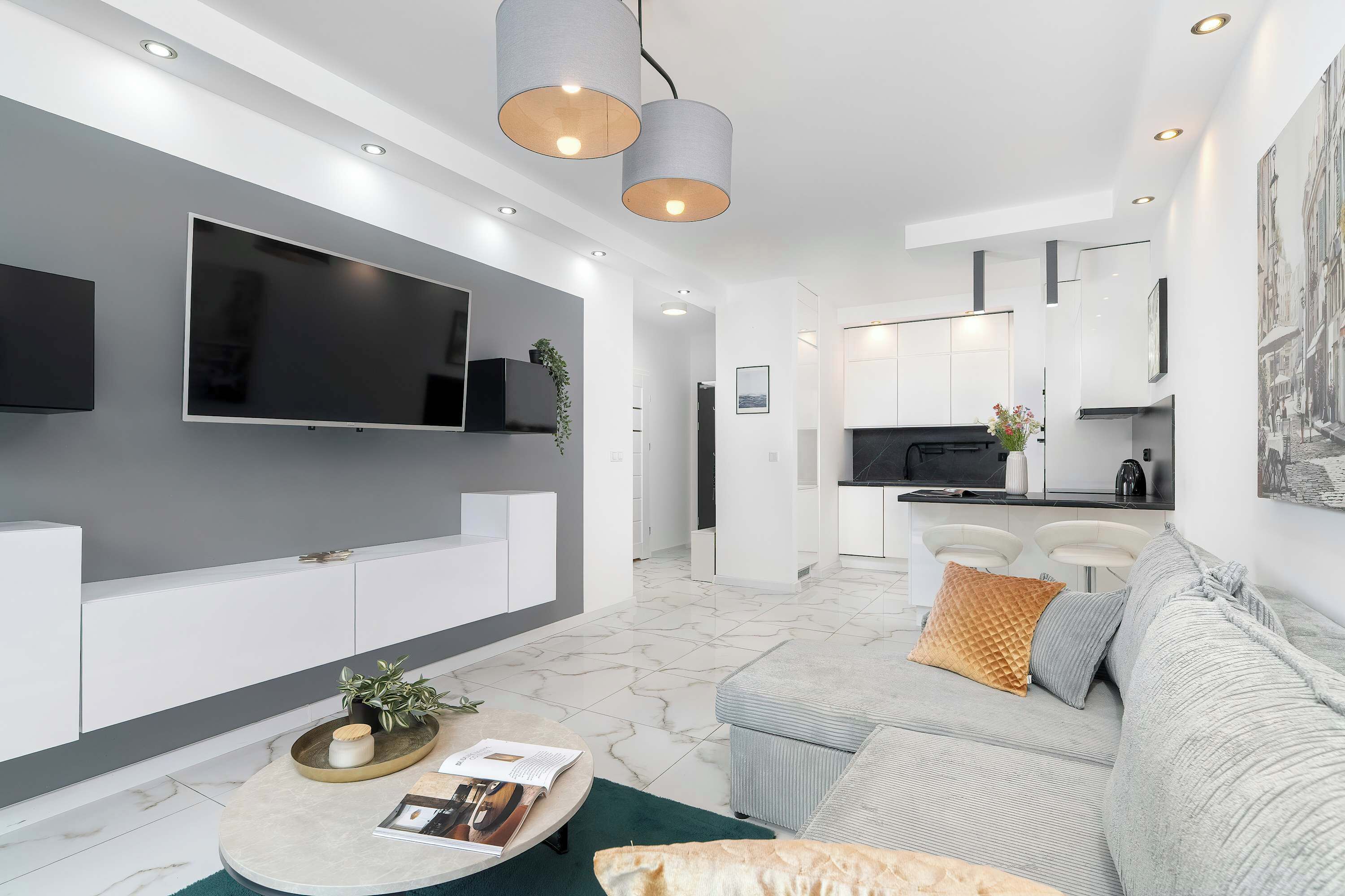 A modern living room with a flat-screen TV, a sofa, a coffee table, and a kitchen area in the background.