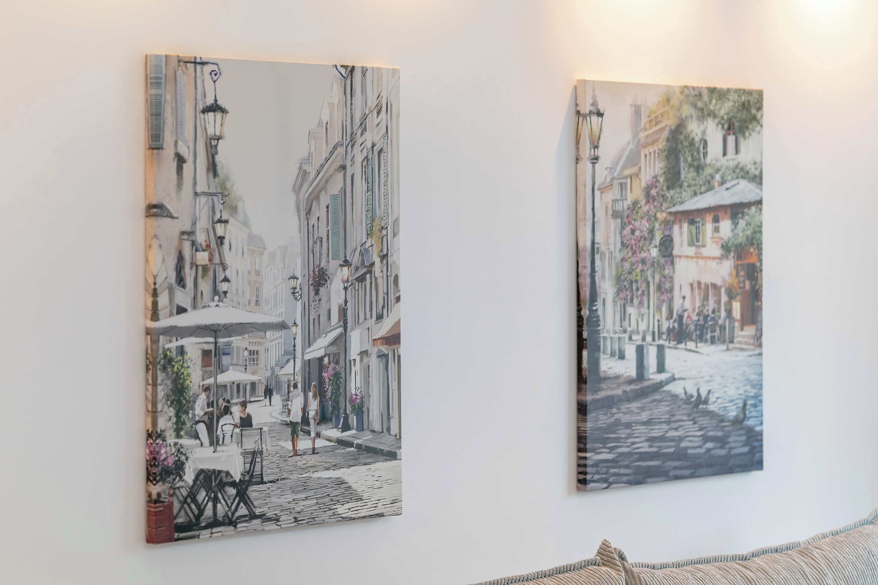 Two framed artworks depicting street scenes on a wall.