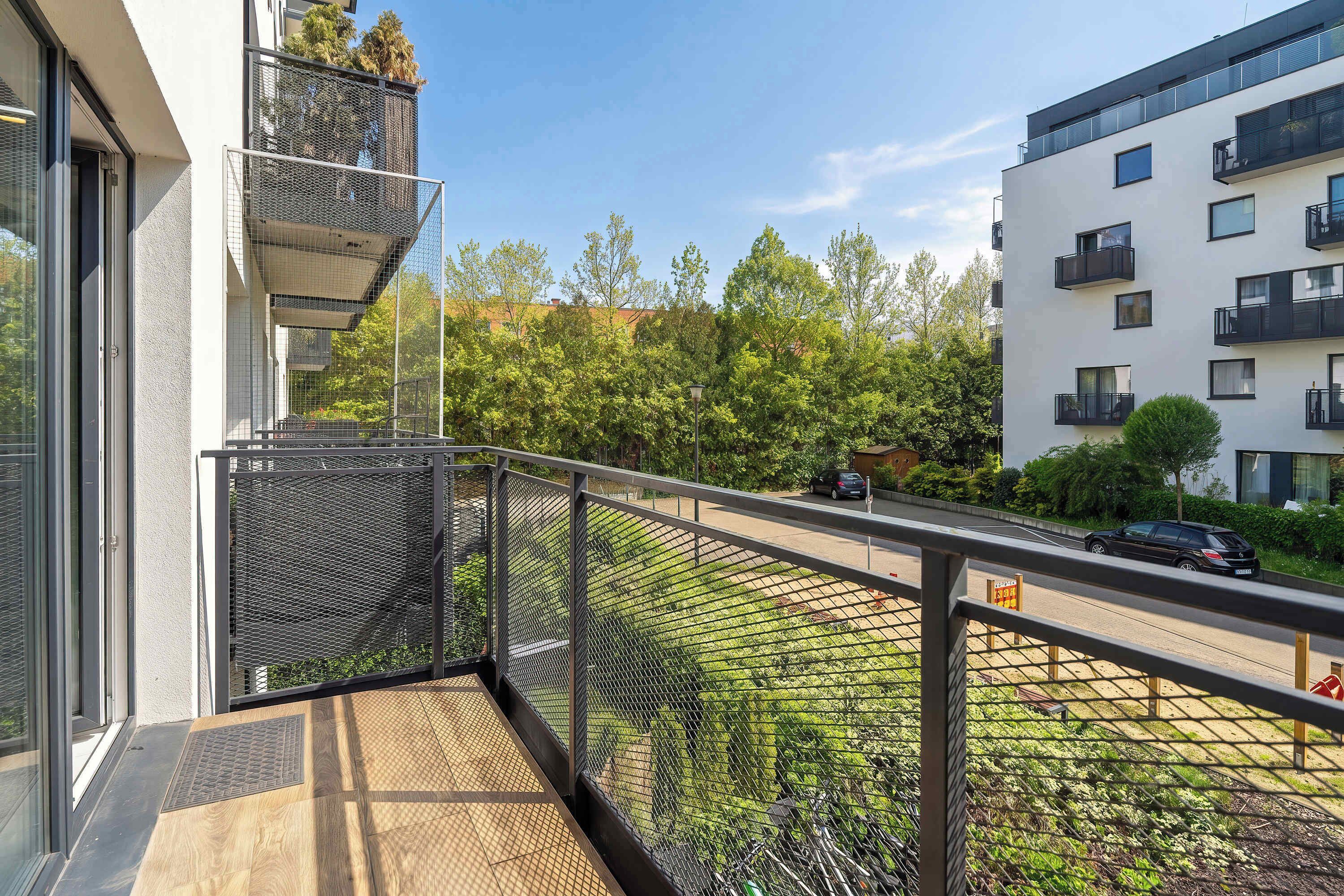 A modern apartment with a balcony, a view of a street, and a neighboring building.