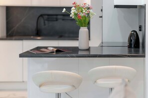 A modern kitchen with a marble countertop, a white vase with flowers, and two white bar stools. - Modern Apartment with a Balcony | Quiet Neighborhood in Poznan (Poznań)