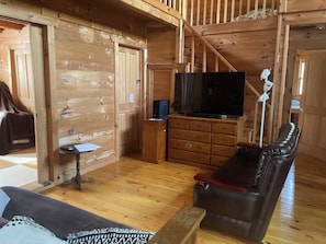 Ein Holzblockhaus-Interieur mit Fernseher, Holzkommode, Ledersofa und einer Treppe.