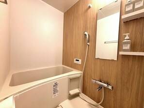 Ett badrum med badkar, en väggpanel av trä, en spegel och en hylla med toalettartiklar.