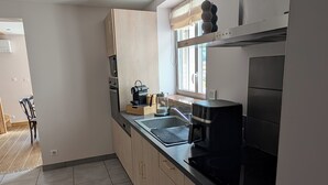 A modern kitchen with a black stove, a sink, and wooden cabinets. - La Mémère bed and breakfast (Le Thillot)