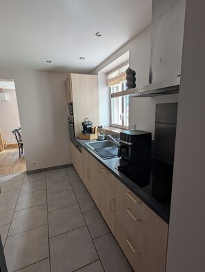 A modern kitchen with a black stove, a sink, and wooden cabinets. - La Mémère bed and breakfast (Le Thillot)