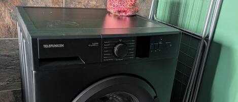 A front-loading washing machine with a control panel, placed in a room with a tiled floor and a green wall.
