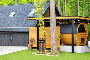 Ein modernes Gebäude mit Garage, ein Hollgebäude mit Fassda und ein Baum im Vordergrund.