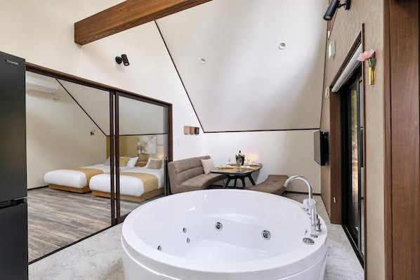 Quarto moderno com cama grande, área de estar e banheiro com banheira espaçosa.