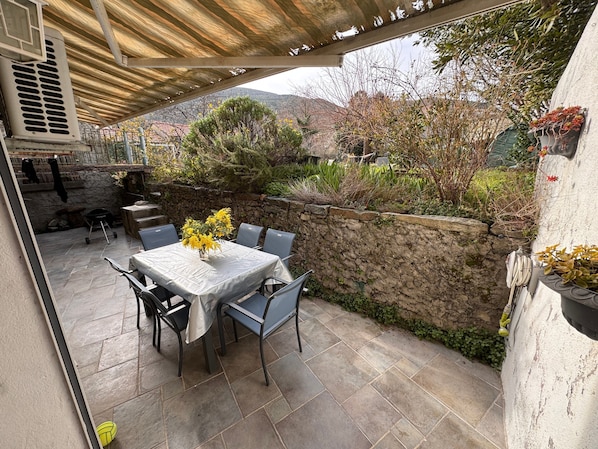 Eine Terrasse im Freien mit Tisch und Stühlen, eine Steinmauer und Blick auf die umliegende Landschaft.