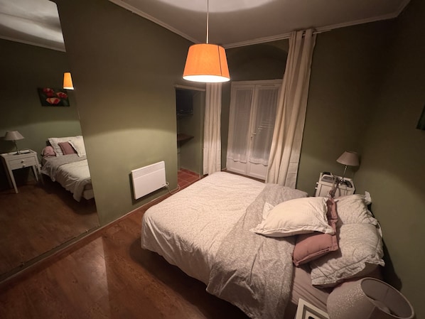 Un dormitorio con cama, lámparas de noche, un radiador, una ventana con cortinas y un espejo.