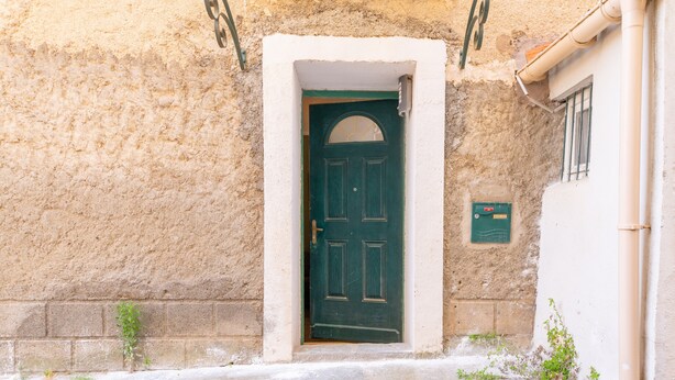 Un edificio con puerta verde, una ventana pequeña y un cuadro eléctrico en la pared.