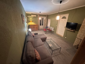 Ein Wohnzimmer mit einer Couch, einem Couchtisch, einem an der Wand befestigten Fernseher und einem Essbereich mit Stühlen und einem Tisch.